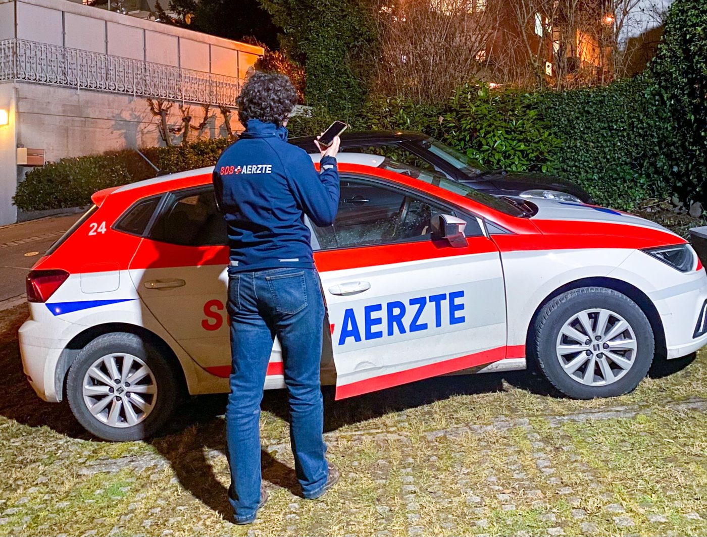 Mitarbeiter von SOS Ärzte Turicum AG am Einsatzfahrzeug, Fallbericht wird auf dem Smartphone diktiert